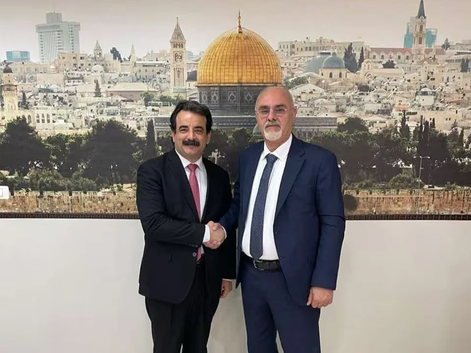 A handshake at the agriculture-ministry meeting in Ramallah, with a Jerusalem panorama behind the participants.