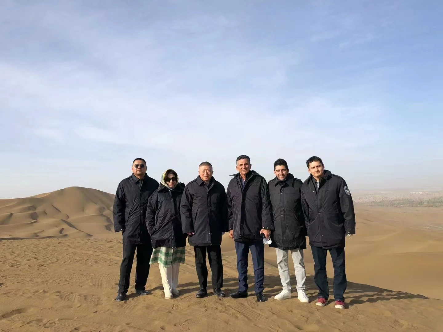 Delegation members stand together in a sandy Xinjiang landscape.