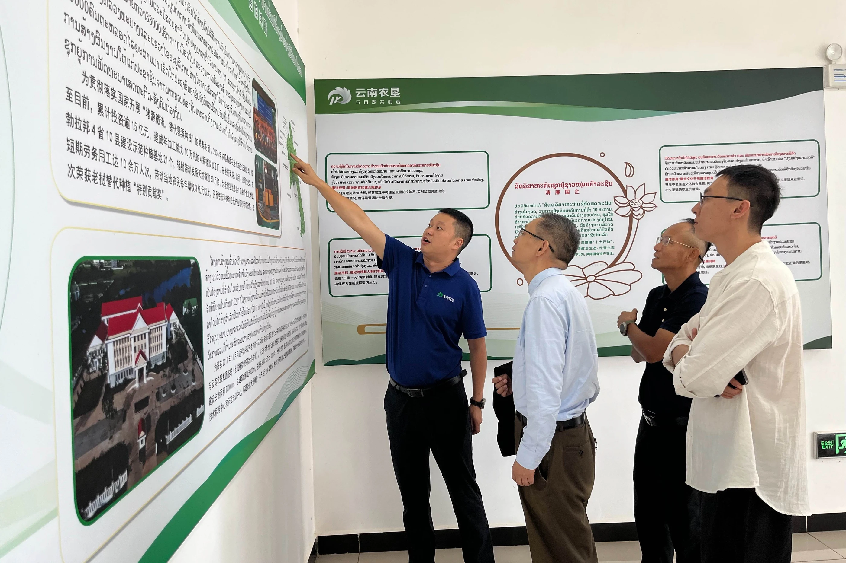 The delegation examines a wall display explaining agricultural cooperation and enterprise activities.