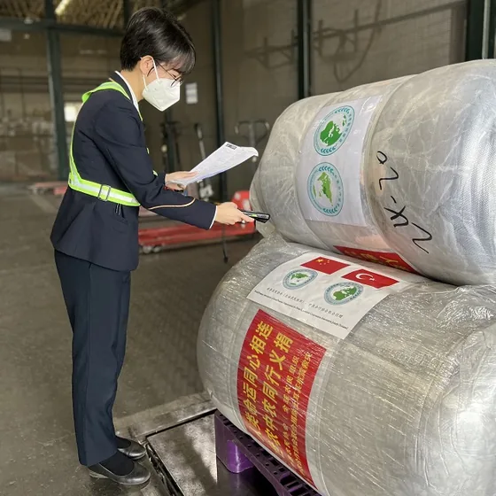 An airport logistics worker checks documentation beside bundled relief supplies.