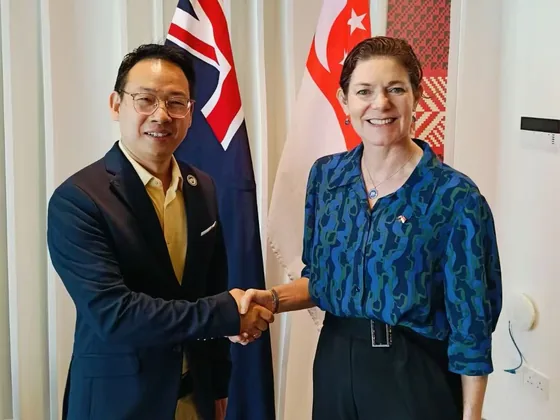 Participants exchange a handshake with New Zealand and Singapore flags in the background.